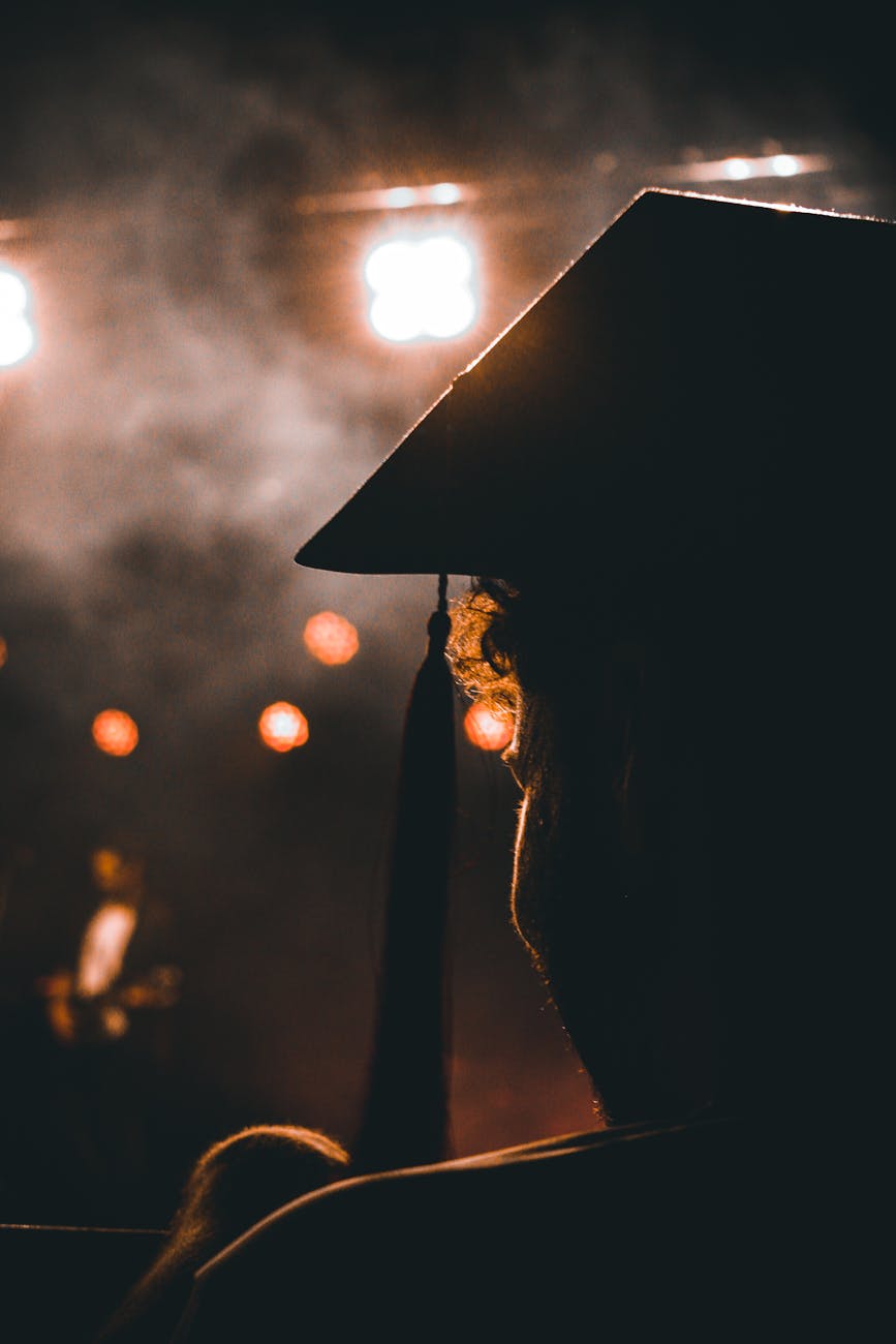 silhouette of a person in a mortarboard looking at an illuminated stage